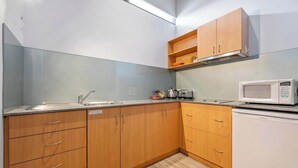 A compact kitchen with wooden cabinets, a microwave, and a sink. - Petra Olive 3 (Yallingup)