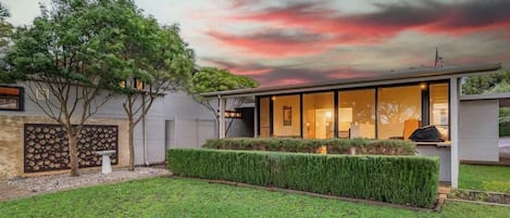 A modern house with a well-maintained lawn, a stone wall, and a large window overlooking the property.