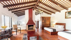 Una habitació àmplia amb un sostre alt, una llar de foc, un llit, un sofà i una zona de dinar amb taula i cadires.
