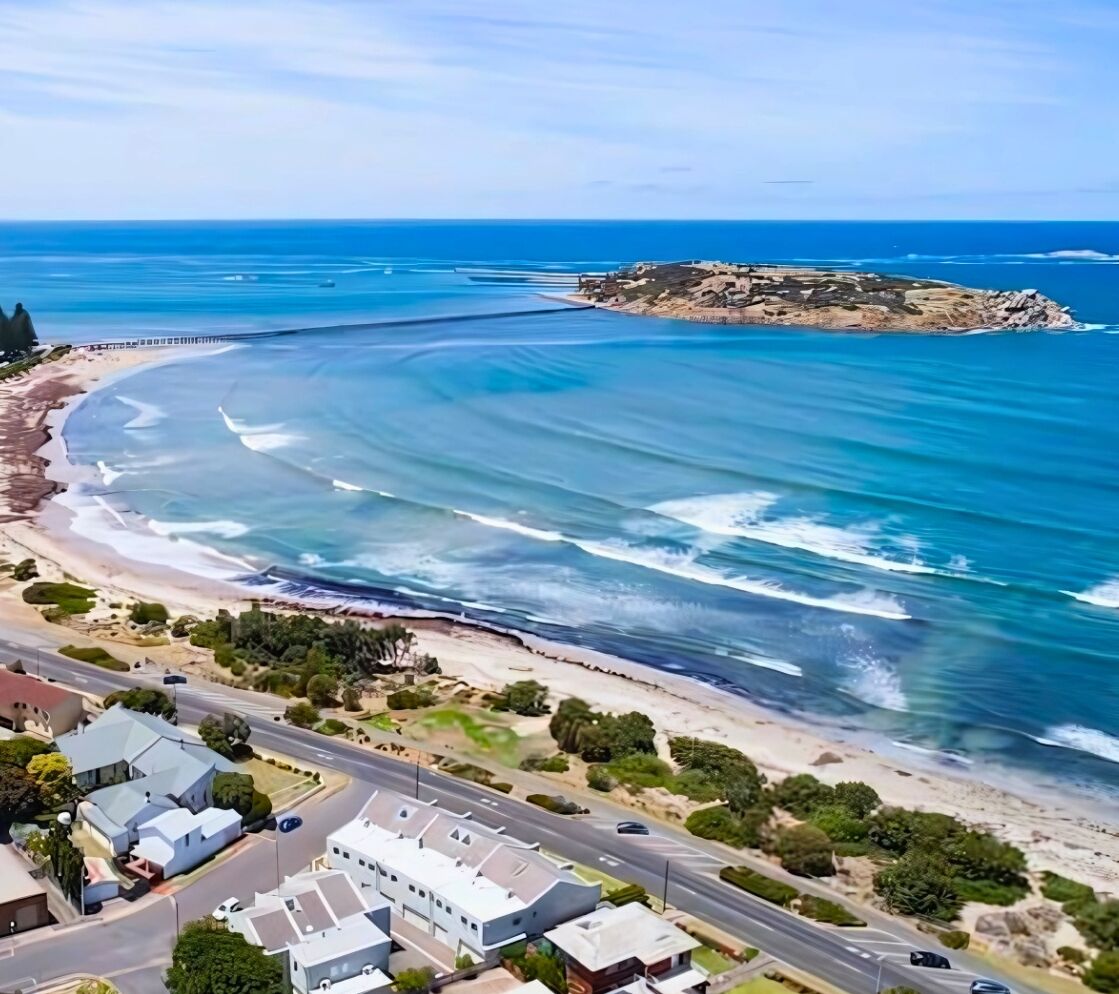 An aerial view of a coastal area with a beach, a rocky outcrop, and residential buildings.