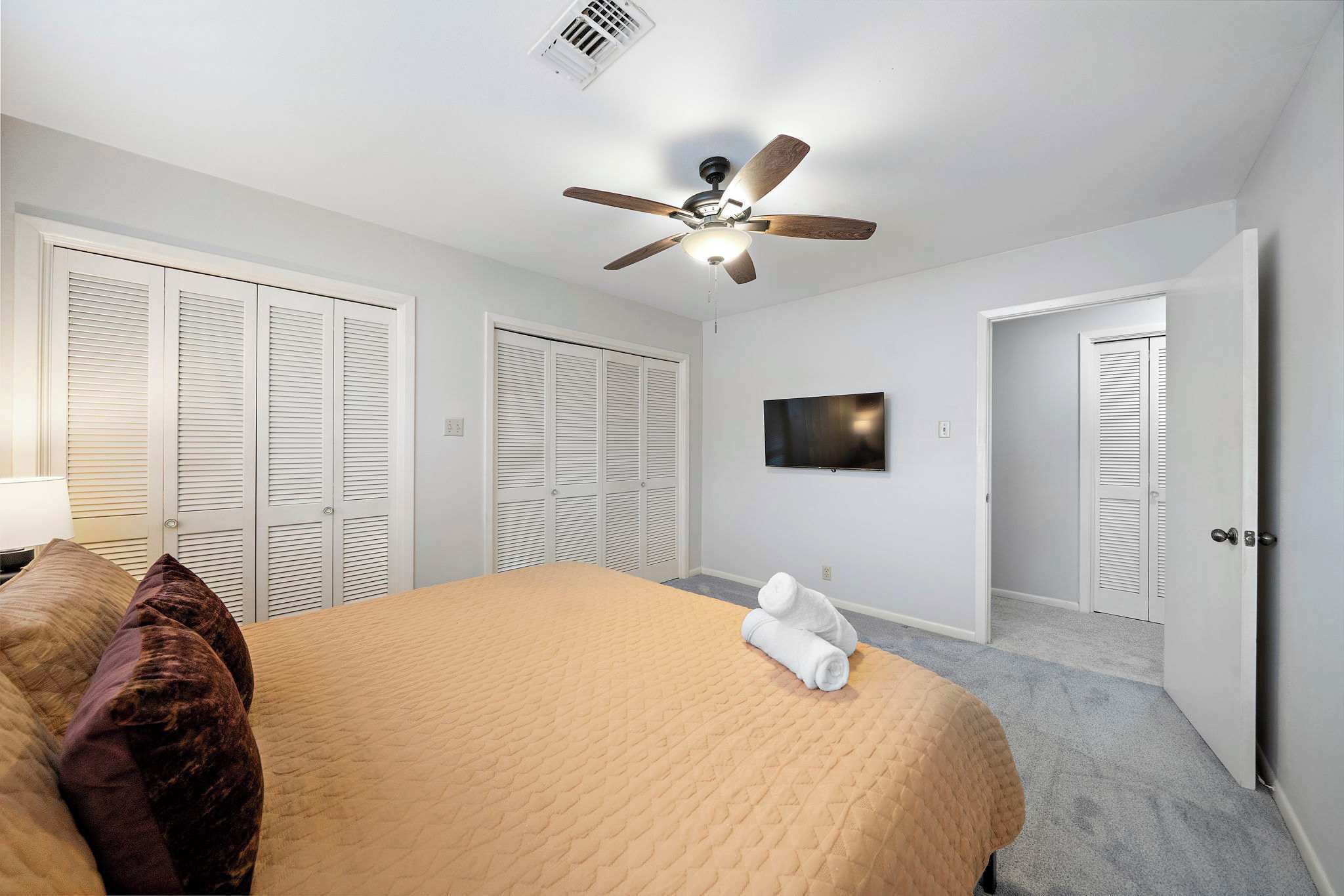 A bedroom with a bed, a ceiling fan, a TV, and white closets.