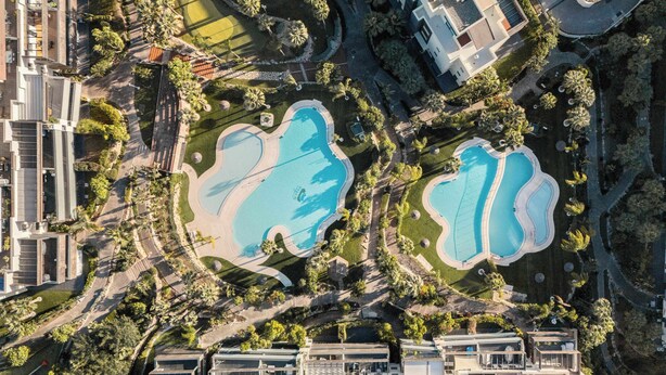 An aerial view of a residential area with two swimming pools, surrounded by greenery and modern buildings.