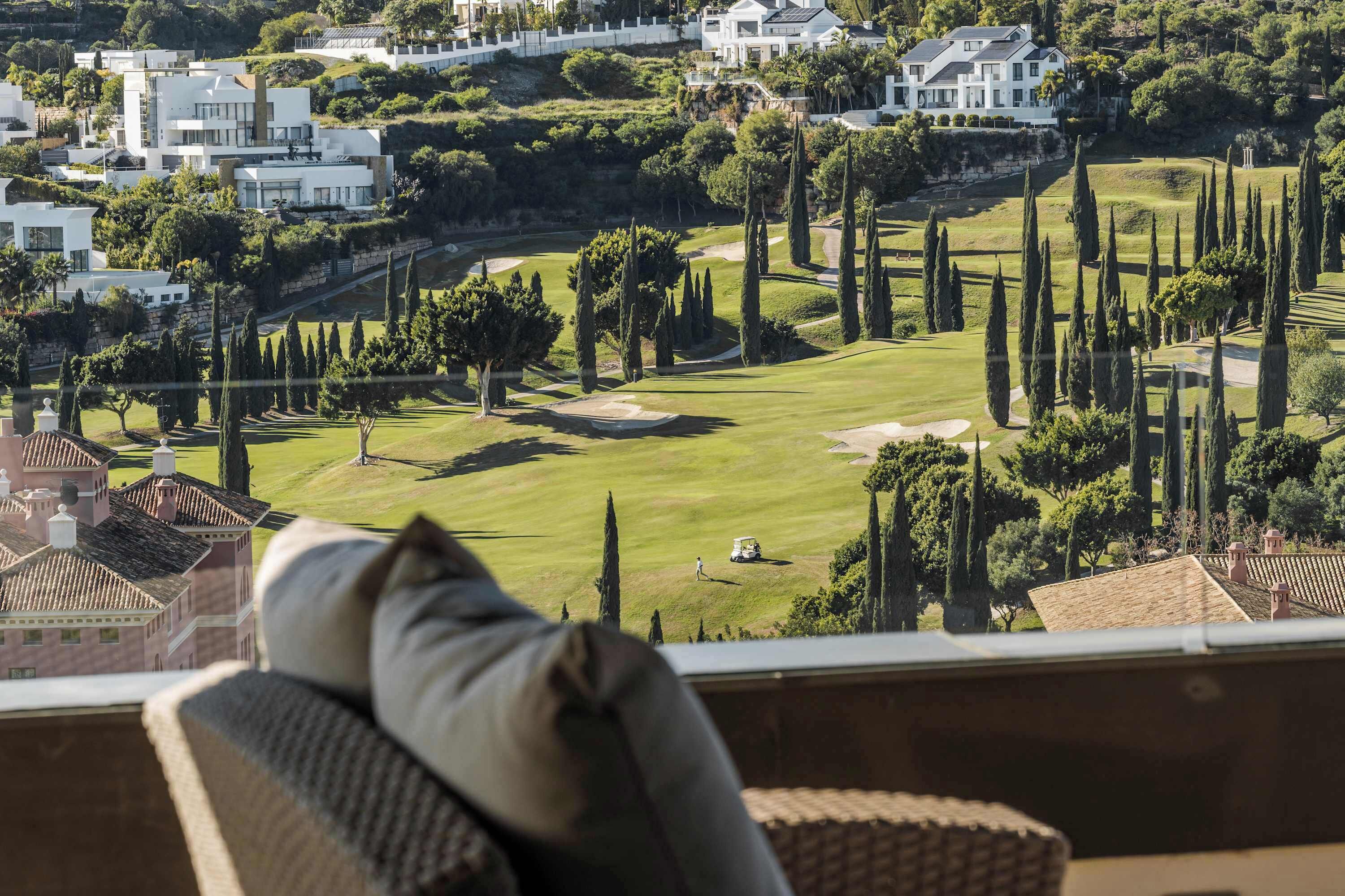 A view from a balcony overlooking a golf course with modern houses in the background.