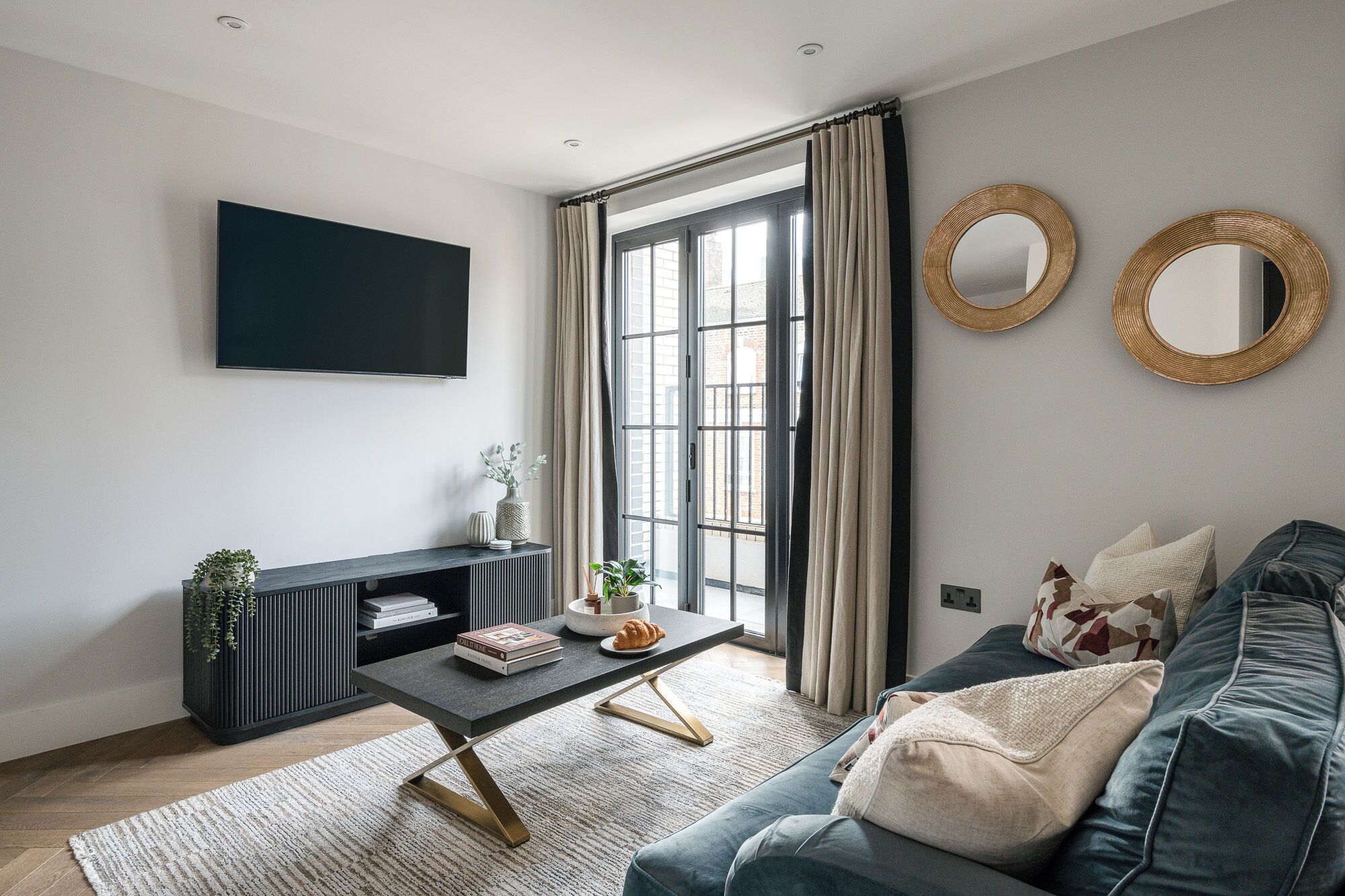 A modern living room with a dark sofa, a coffee table, a TV, and a large window with curtains.