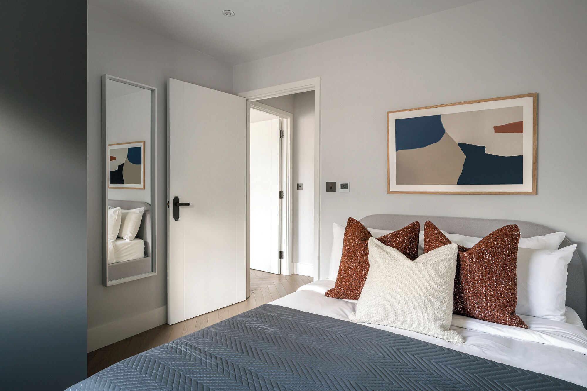 A modern bedroom with a bed, a door, a mirror, and abstract art on the wall.