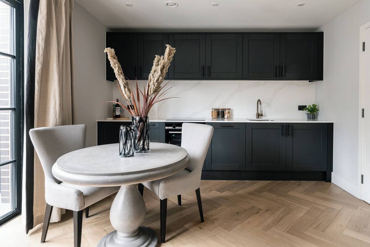 Una cocina moderna con armarios oscuros, encimera de mármol y una mesa de comedor redonda con sillas.