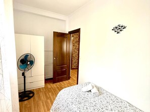 Un dormitorio con cama, ventilador, armario y una puerta que da a otra habitación.