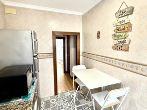 Una cocina con refrigerador, una mesa de comedor con sillas y una pared decorada con letreros motivacionales.