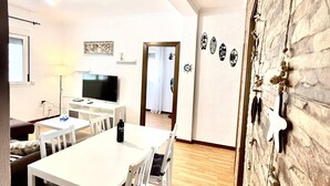 Uma sala de estar moderna com televisão de tela plana, uma mesa de jantar com cadeiras, um sofá e um abajur.