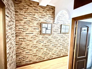 A hallway with a textured stone wall, framed pictures, and a wooden door with a sign.