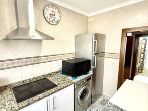 A compact kitchen with a built-in microwave, a stainless steel range hood, a washing machine, and a clock on the wall. - Los 3 hermanos by Staycare (Rota)