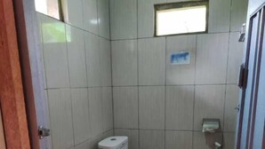 A small, tiled bathroom with a toilet, a window, and a patterned floor. - Roemah Abdoe (Harau)