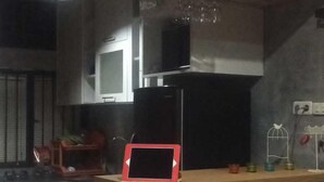 A kitchen with white cabinets, a microwave, and a tablet on a wooden shelf. - Roemah Abdoe (Harau)