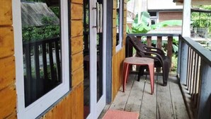 A wooden porch with a table and chairs, a red mat, and a view of greenery and a building in the background. - Roemah Abdoe (Harau)
