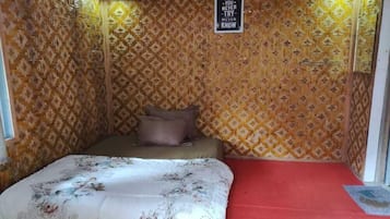 A small, cozy room with a patterned wallpaper, a bed with floral bedding, and a red carpet.