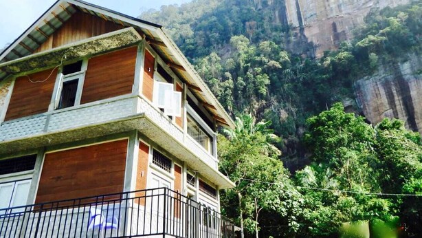 A two-story building with a balcony, set against a backdrop of a steep cliff and dense forest. - Roemah Abdoe (Harau)