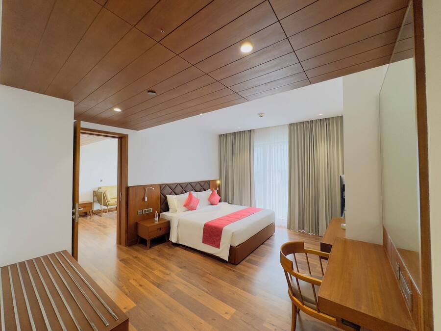A modern hotel room with a wooden ceiling, a large bed with white and pink pillows, a wooden desk, and a television.