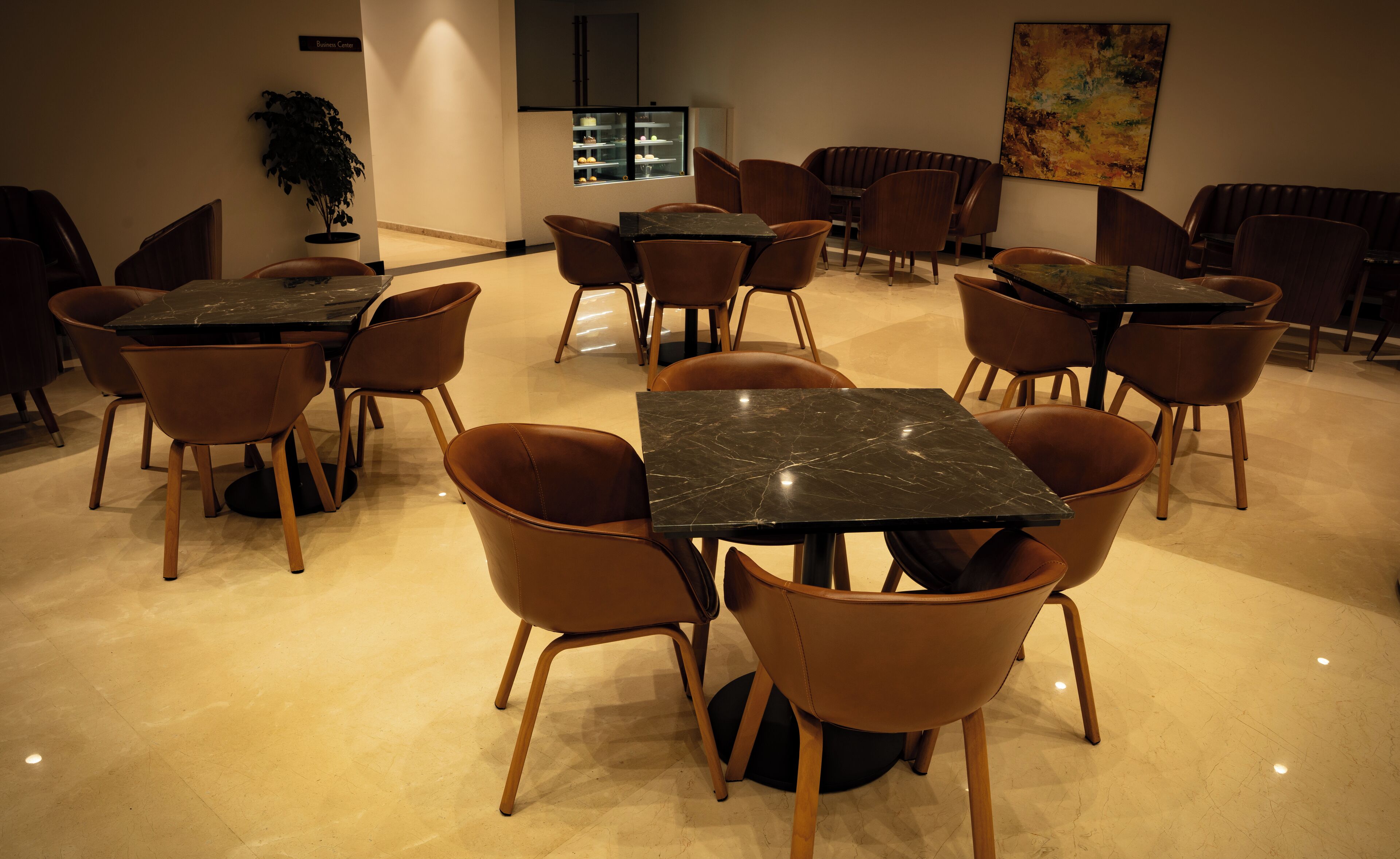 A dining area with multiple tables and chairs, a potted plant, and a dessert display.