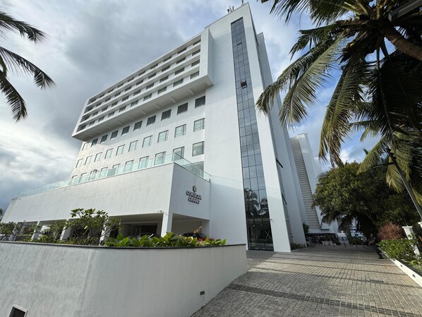 A modern building with a prominent entrance, multiple floors, and a surrounding landscaped area with palm trees. - Gokulam Grand Kozhikode (Kozhikode)