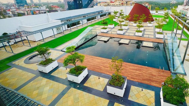 A rooftop pool area with a glass barrier, potted plants, and a view of the cityscape. - Gokulam Grand Kozhikode (Kozhikode)