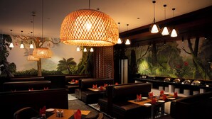 A restaurant with booths and tables, warm lighting, and a jungle-themed mural. - Gokulam Grand Kozhikode (Kozhikode)