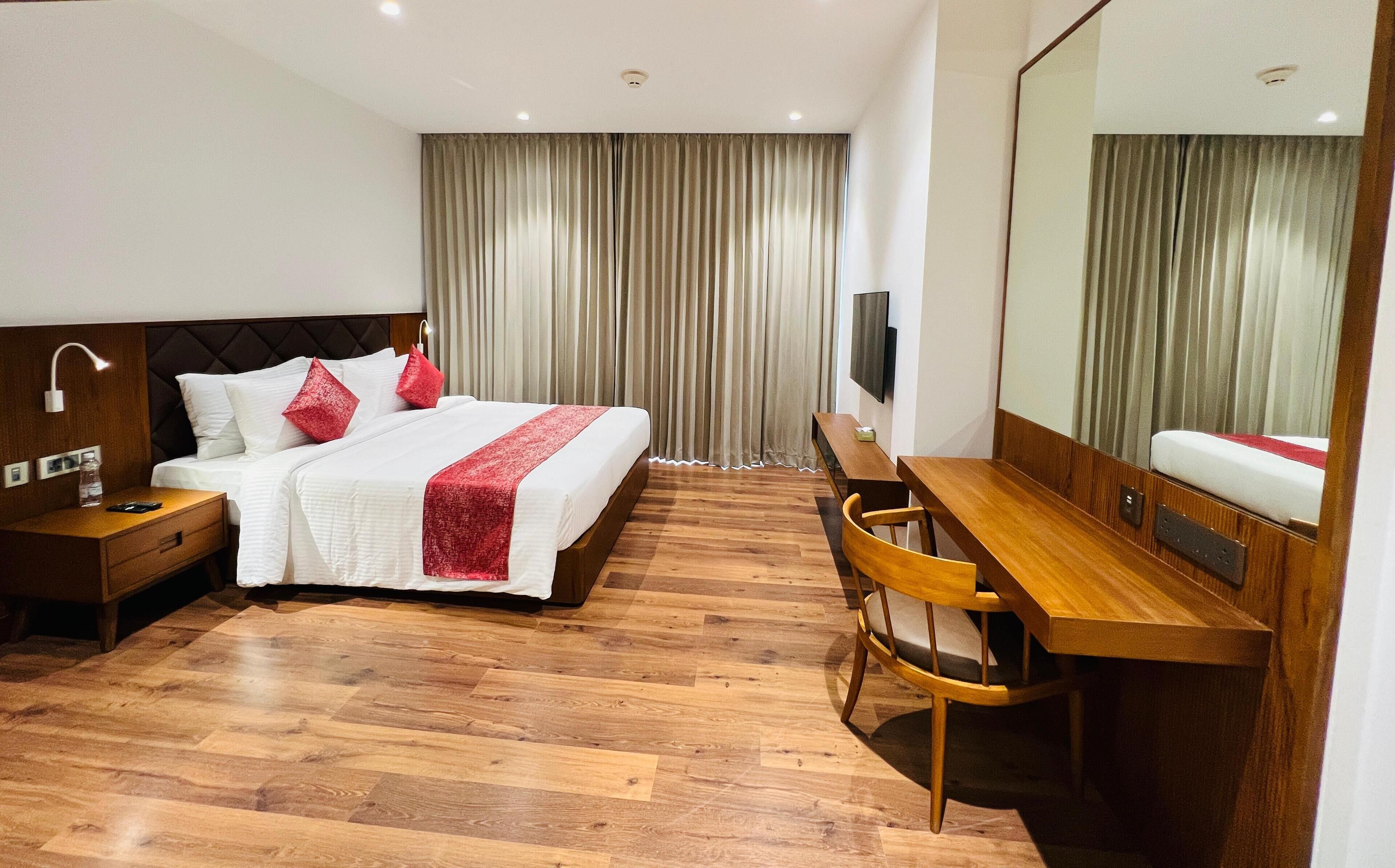 Habitación de hotel con cama, escritorio, silla, televisor y espejo.