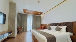 A modern hotel room with a large bed, wooden flooring, a flat-screen TV, and a dining area with chairs. - Gokulam Grand Kozhikode (Kozhikode)