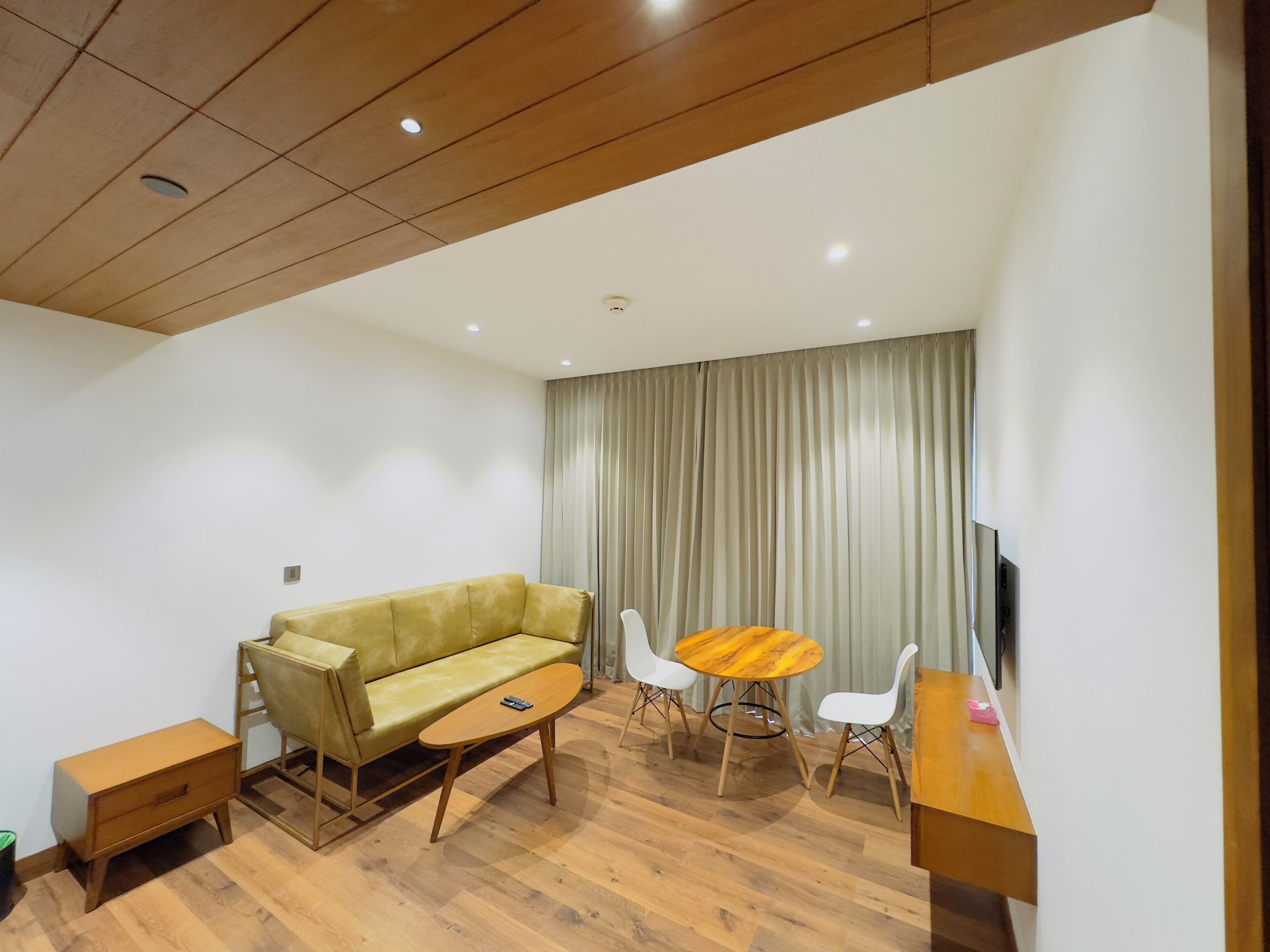 A modern living room with a sofa, a coffee table, a TV, and a dining area with chairs and a table.