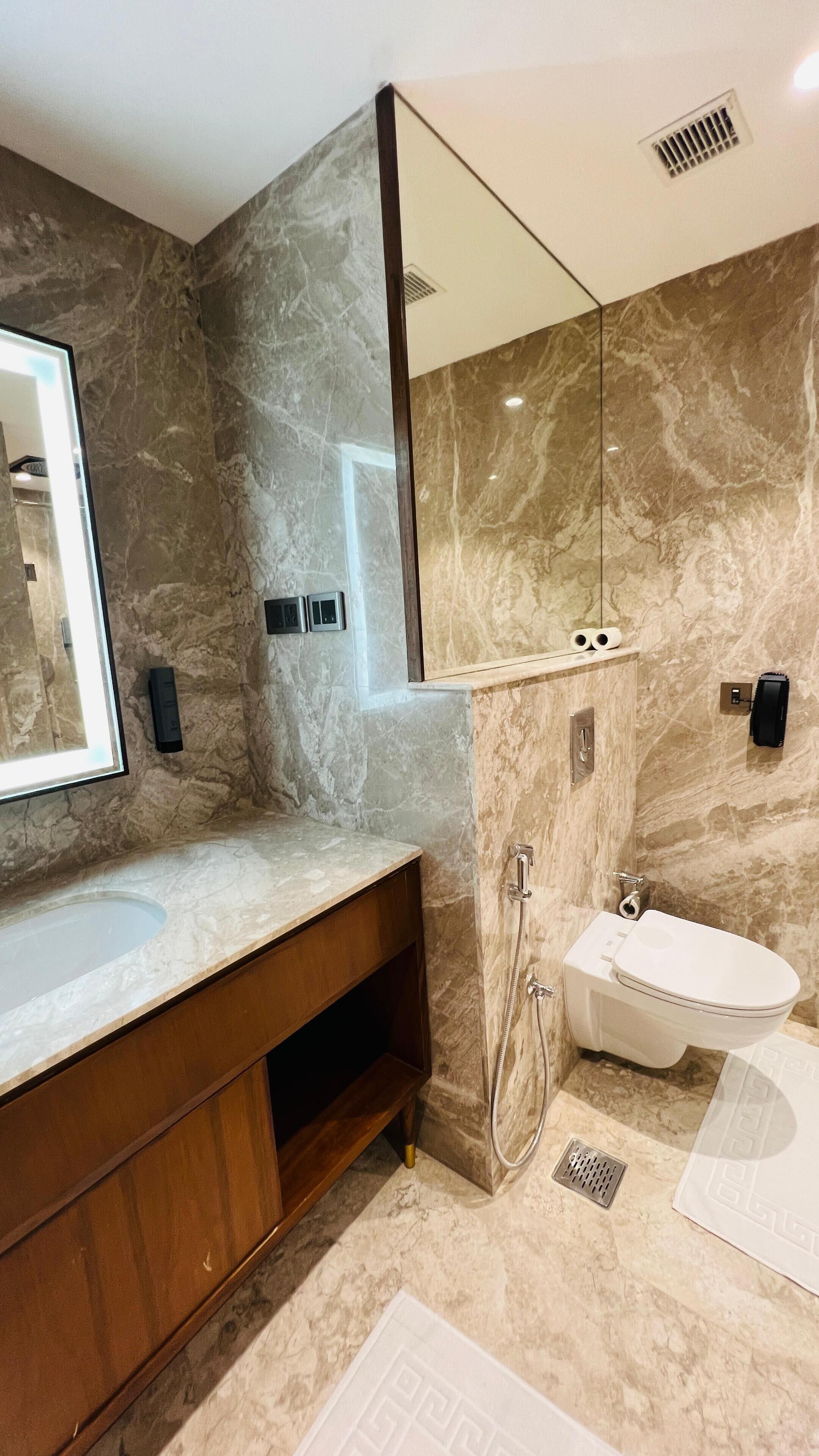 Une salle de bain moderne avec un meuble-lavabo en marbre, un grand miroir, un lavabo encastré, des toilettes et une douche.