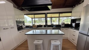 A modern kitchen with white cabinets, a central island with stools, and large windows offering a view of the outdoors. - 3 Bdrm Farm Stay with Goats, Hairy Coos and chickens. Farm Life. You'll Love it! (Postmans Ridge)