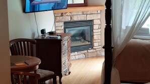 A living room with a television mounted on the wall, a fireplace, a dining table with chairs, and a bed with a canopy. - Cozy studio in nice Piedmont with AC, WiFi, parking, kitchenette (Piedmont)