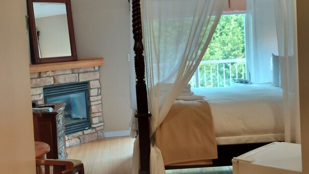 A bedroom with a four-poster bed, a stone fireplace, and a view of greenery outside. - Cozy studio in nice Piedmont with AC, WiFi, parking, kitchenette (Piedmont)