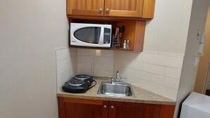 A small kitchen with wooden cabinets, a microwave, a stove, and a sink. - Cozy studio in nice Piedmont with AC, WiFi, parking, kitchenette (Piedmont)