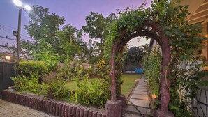 Un sendero de jardín con un arco de madera, rodeado de abundante vegetación y un césped bien cuidado.
