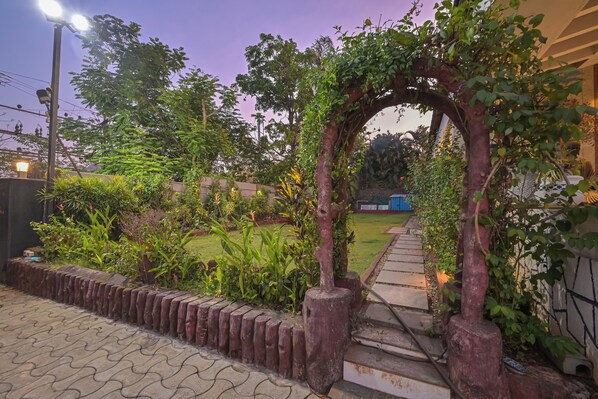 A garden pathway with a wooden archway, surrounded by lush greenery and a well-maintained lawn.