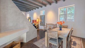 A dining area with a wooden table and chairs, a vase with flowers, and a window with a view of trees. - Striking Design, Fireplaces, Roof Deck (Santa Fe)