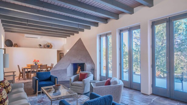 A modern living room with a stone fireplace, large windows, and a dining area. - Striking Design, Fireplaces, Roof Deck (Santa Fe)