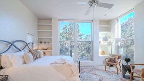 A bedroom with a bed, a ceiling fan, a large window, and a view of trees. - Striking Design, Fireplaces, Roof Deck (Santa Fe)