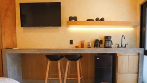 Una cocina compacta con una televisión de pantalla plana, taburetes de madera, una cafetera y un refrigerador.