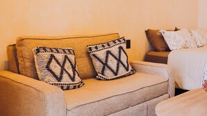 Un sofá color beige con cojines estampados, una mesita redonda pequeña y un adorno colgante en la pared.