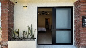 Una entrada moderna con una puerta de cristal corredera que da a un dormitorio con una cama y un ventilador de techo.