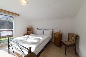 A bedroom with a bed, a chair, a nightstand, a wooden cabinet, and a window with a view of a green landscape.