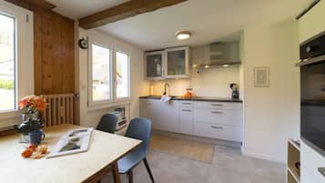 Ett modernt kök med vita skåp, en inbyggd ugn och en matplats med bord och stolar.