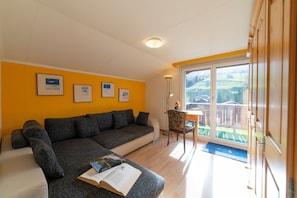 A living room with a sofa, a table, and a chair. There are framed pictures on the wall.