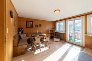 A cozy room with a wooden bench, a dining table, and chairs. There is a bookshelf and a radiator.