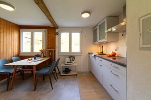 A compact kitchen with a dining area, wooden walls, and a window providing natural light.