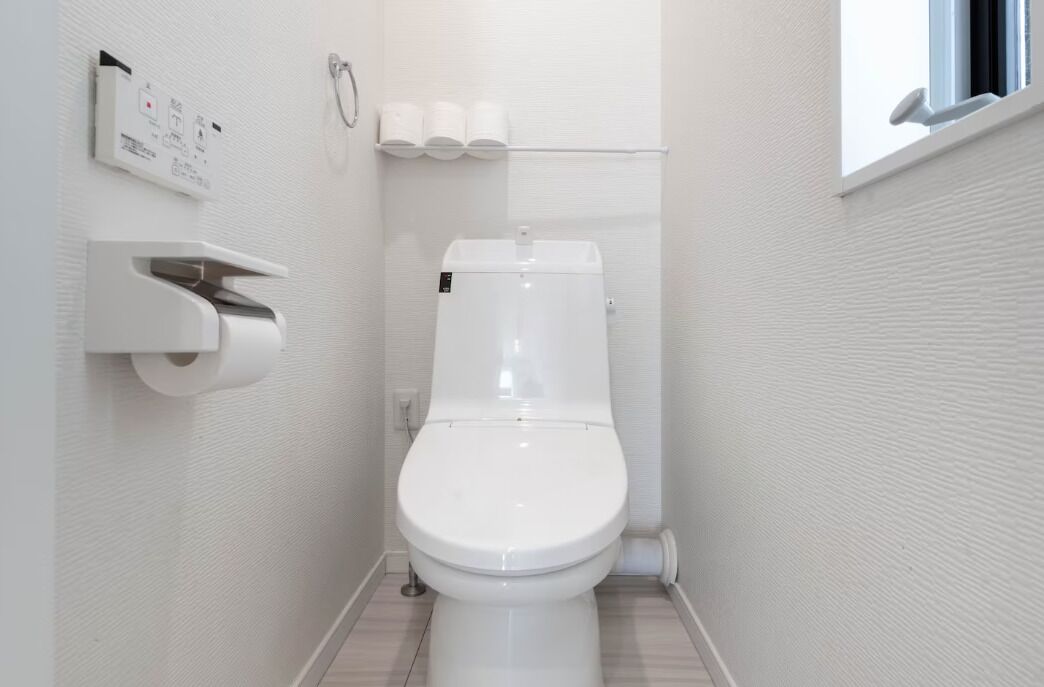A small, modern bathroom with a toilet, a paper towel dispenser, and a toilet paper holder.