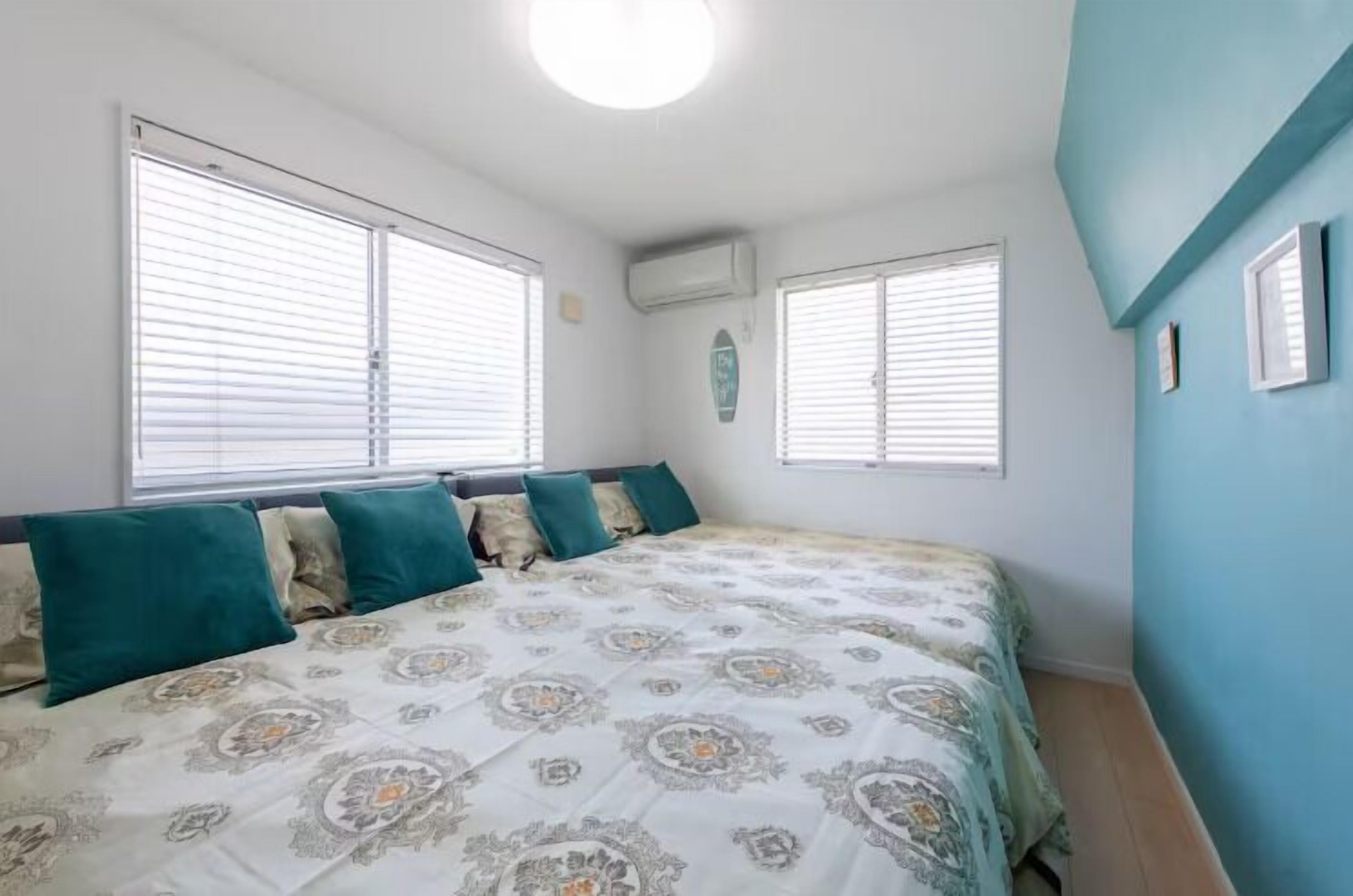 A bedroom with a bed, two windows, and a wall-mounted air conditioner.