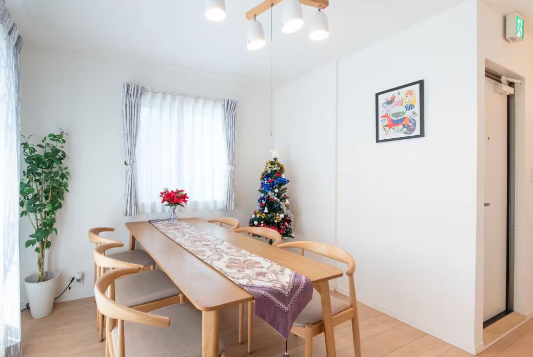 A dining area with a wooden table and chairs, a Christmas tree, and a potted plant.