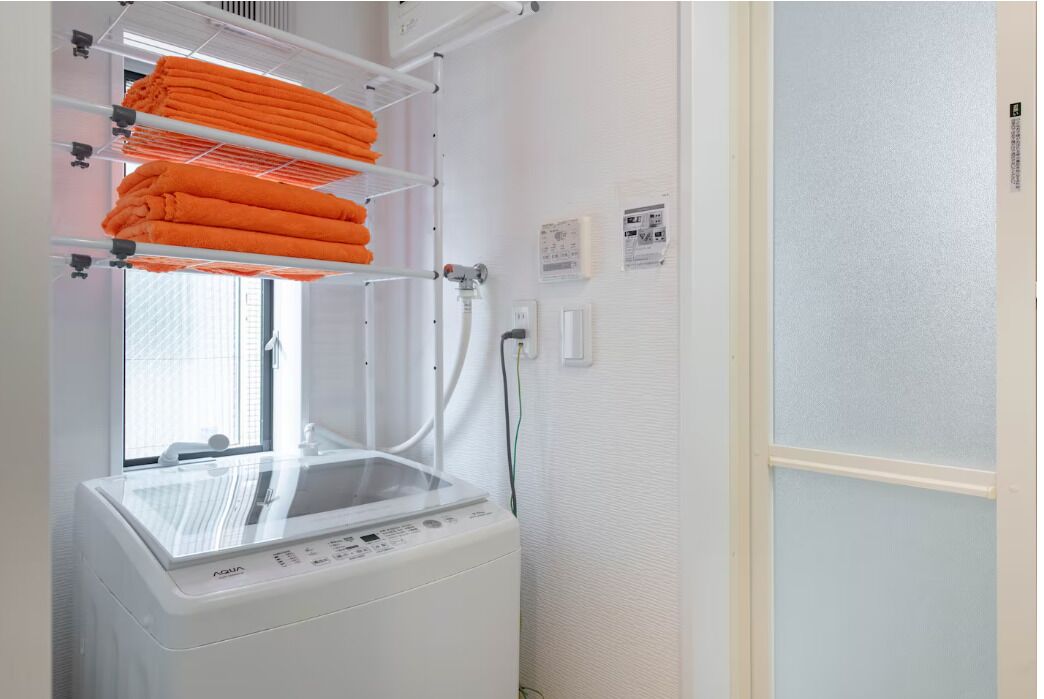 A laundry room with a white washing machine and a drying rack with orange towels.